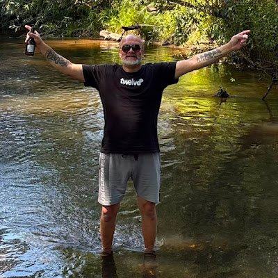 Ich stehe mit ausgebreiteten Armen und Sonnenbrille mitten in einem Fluss.